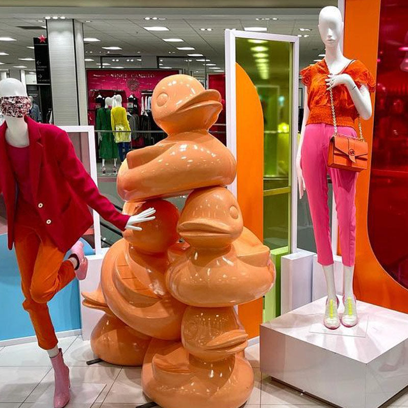 A stack of orange duck sculptures in a Macy's fashion display.