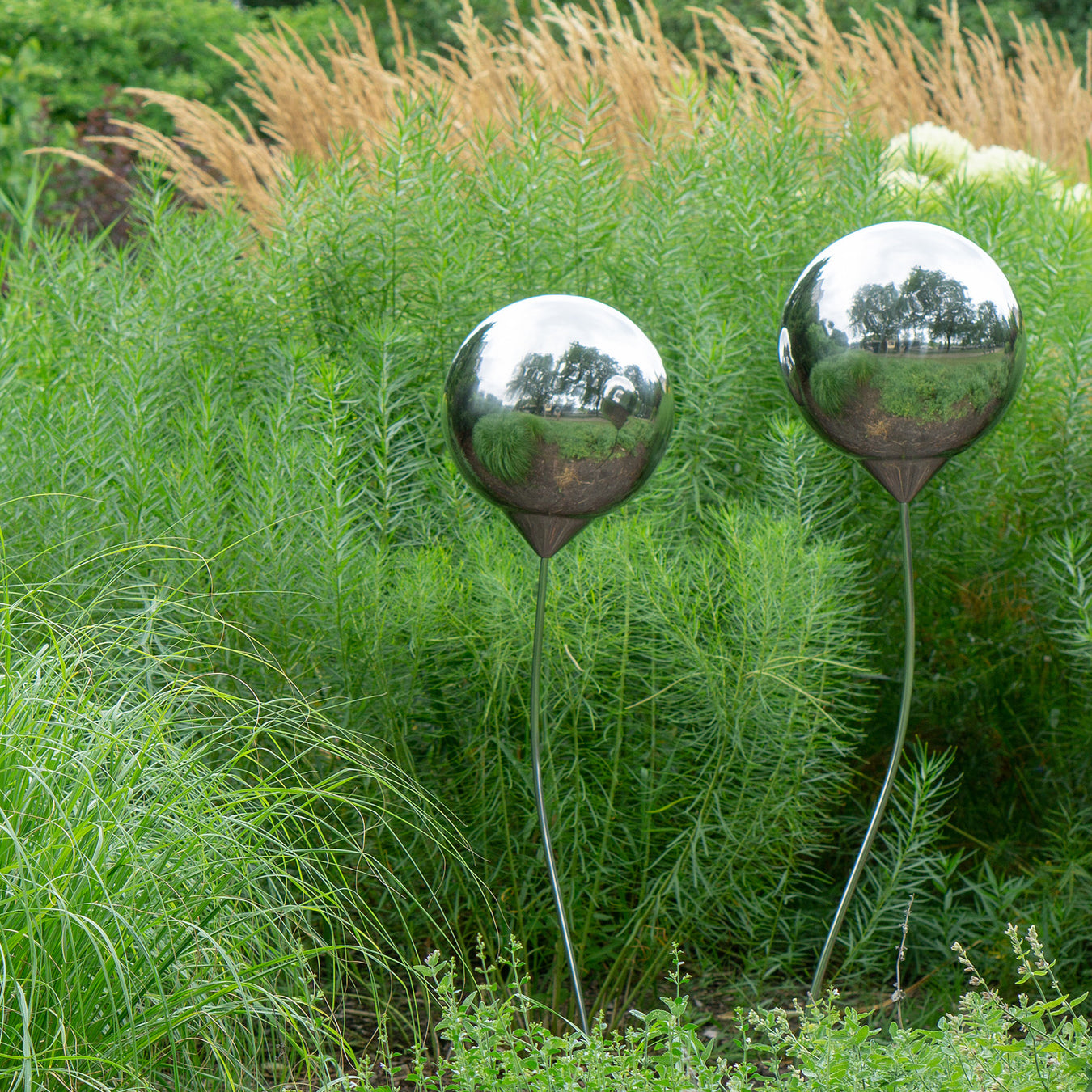 Two stainless steel sculptures by grasses outdoors.