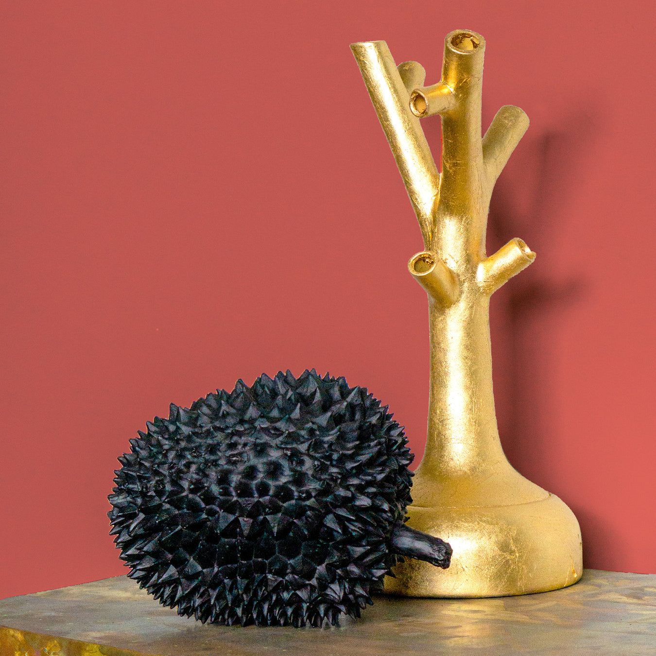 Black Durian sculpture next to a gold leaf Shinzo Tree sculpture against a red wall.