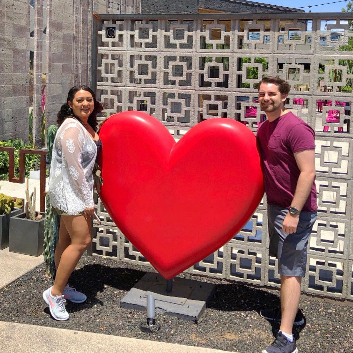 Two people standing next to a large red heart sculpture.