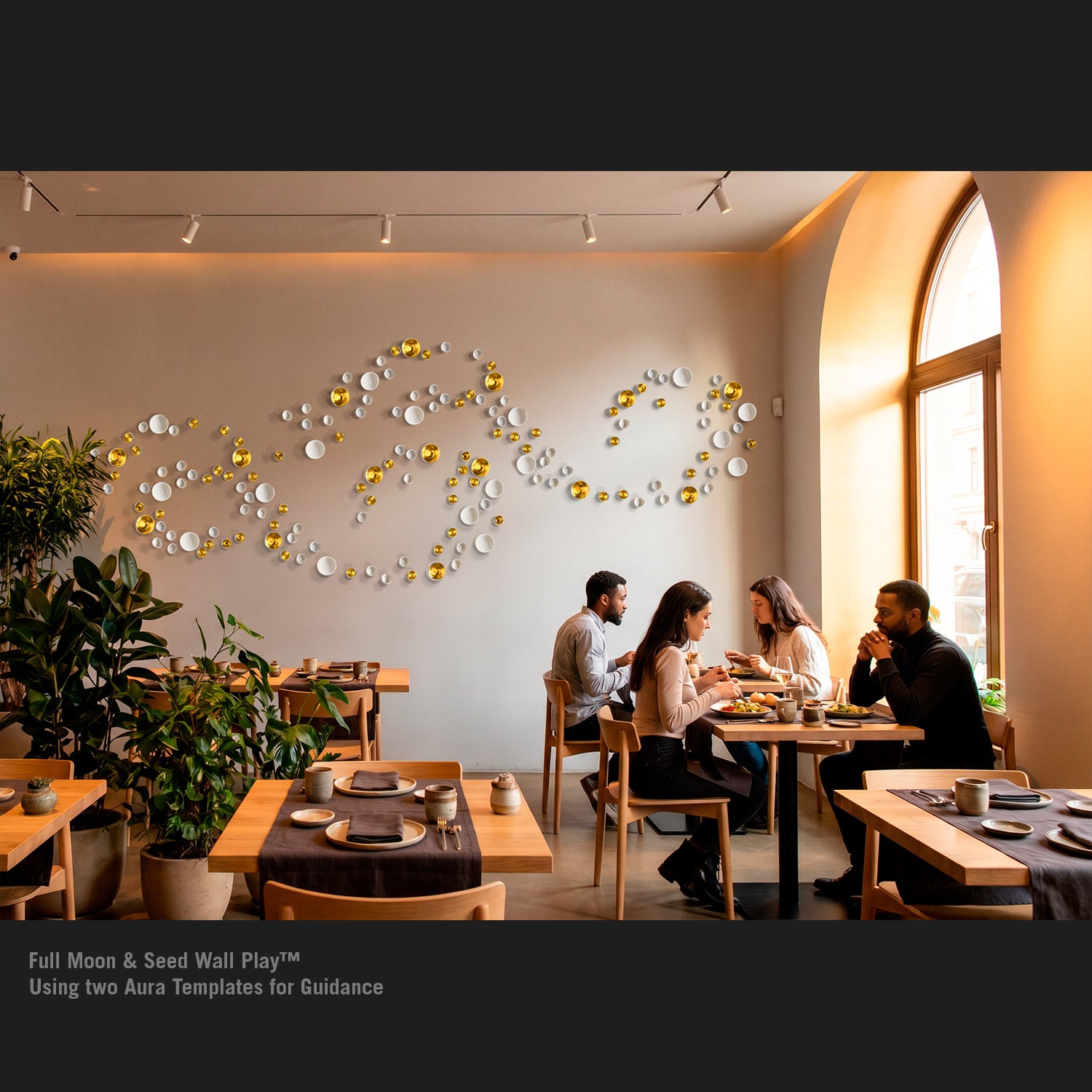 A modern restaurant interior with several people seated at tables near a large arched window. On the wall, a decorative arrangement of white and gold circular Wall Play sculptures.