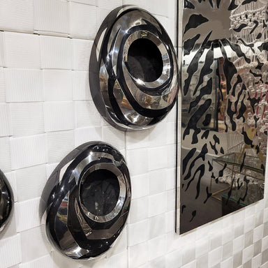 Two different sized 3-D Velocity Wall Art  handcrafted of polished stainless steel and black resin in swirl pattern. Mounted on woven white fabric wall with black and stainless steel Vein Wall Art hanging next to them. 