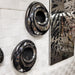 Two different sized 3-D Velocity Wall Art  handcrafted of polished stainless steel and black resin in swirl pattern. Mounted on woven white fabric wall with black and stainless steel Vein Wall Art hanging next to them. 